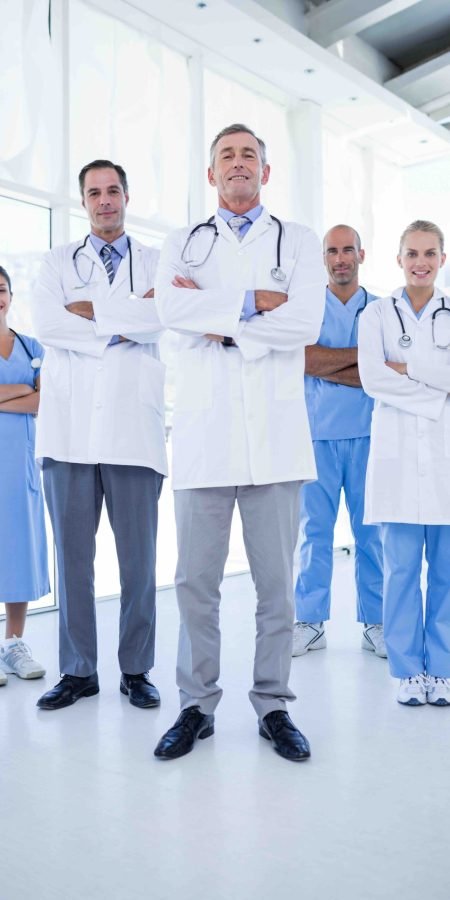 Team of smiling doctors looking at camera with arms crossed in medical office